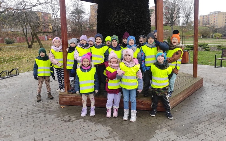 Grupa dzieci w żółtych kamizelkach na placu zabaw.