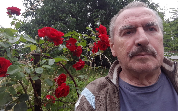 Mężczyzna z różami w tle, uśmiechający się do kamery.