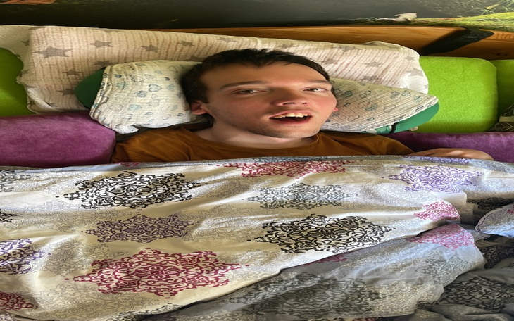 Młody mężczyzna leżący w łóżku, przykryty kocem.