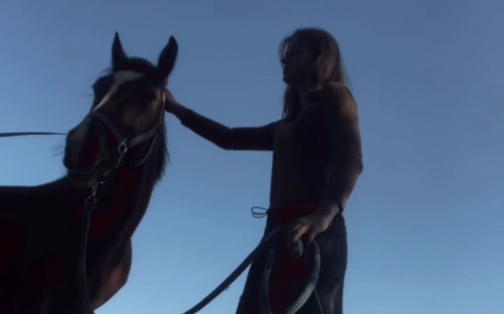 Osoba głaszcząca konia na tle nieba.