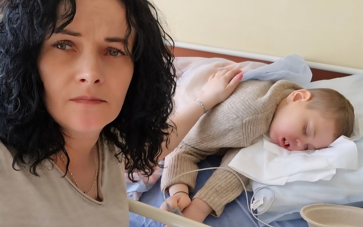 Chłopiec śpiący w szpitalnym łóżku z opiekunem obok.