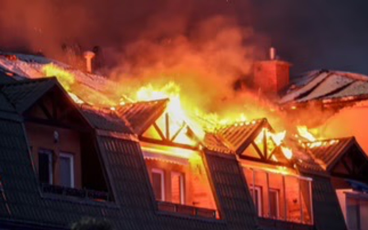Dach płonącego budynku, ogień i dym w nocy.