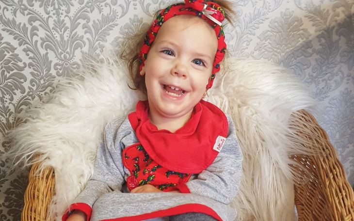 Mała dziewczynka w kolorowej sukience, uśmiechająca się.