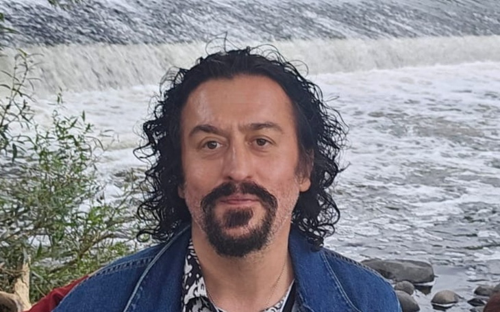 Mężczyzna z kręconymi włosami przy wodospadzie.