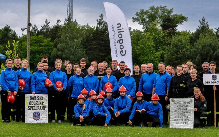 Grupa strażaków w niebieskich strojach na tle flagi.