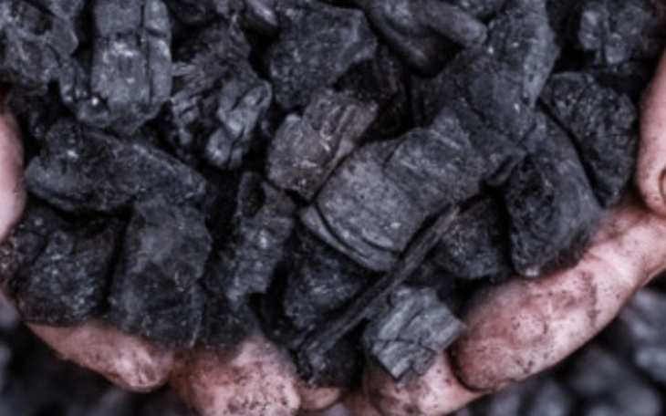 Ręce trzymają węgiel, symbolizujący trudną pracę i wysiłek.