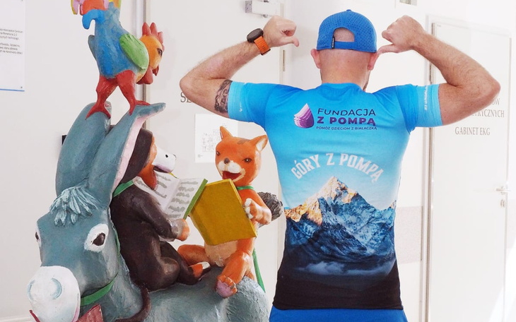 Mężczyzna w koszulce z fundacji, pozujący z rzeźbą.