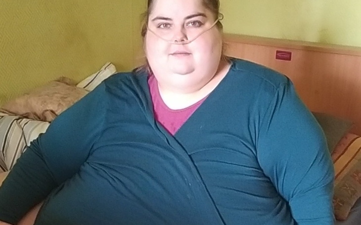 Kobieta siedzi na łóżku, z tlenem na nosie, w zielonej bluzie.