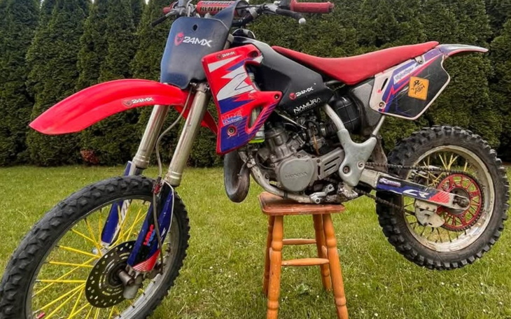 Motocykl terenowy stojący na stołku w ogrodzie.