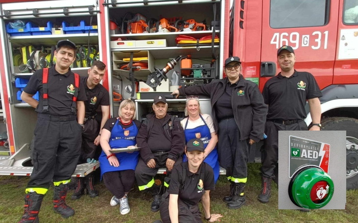 Grupa ratowników w mundurach, pozująca przy wozie strażackim.