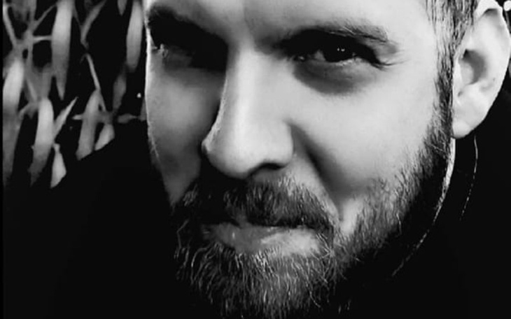 Czarnobiałe zdjęcie mężczyzny z brodą, uśmiechającego się tajemniczo.