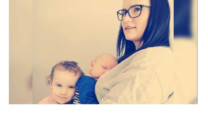 Mama z dwójką dzieci, jedno na rękach, uśmiechnięte.