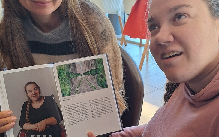 Dwie kobiety trzymają książkę z ilustracją i tekstem.