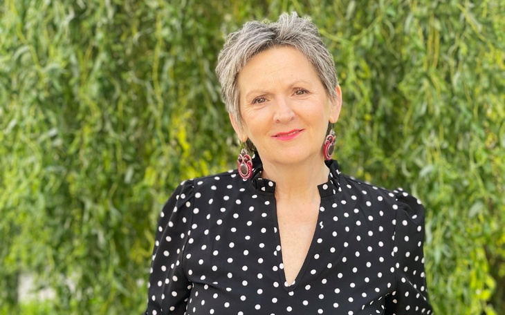 Kobieta w czarnej bluzce w kropki, uśmiechająca się na tle zieleni.