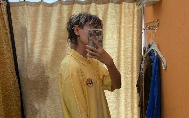 Młoda osoba w żółtej koszuli, robiąca selfie w lustrze.