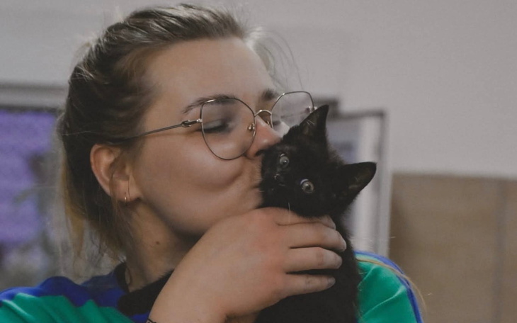 Kobieta całuje małego czarnego kotka.