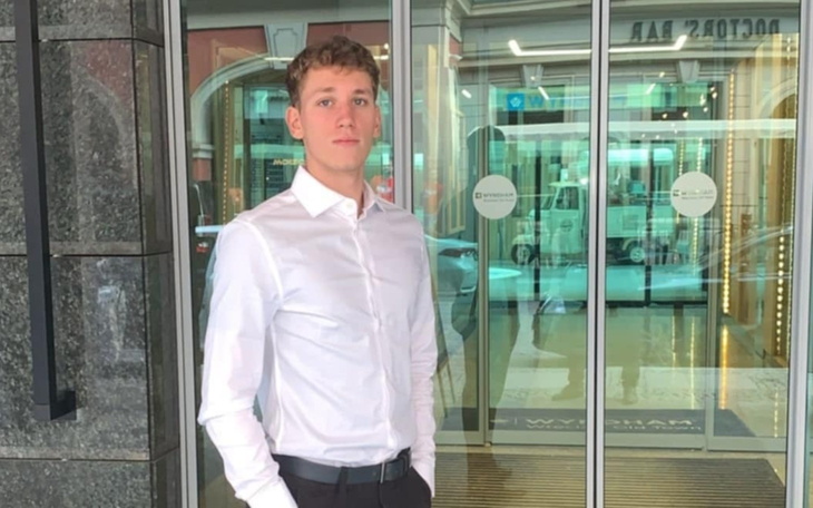 Młody mężczyzna w białej koszuli przy szklanych drzwiach.