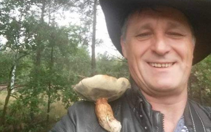 Mężczyzna z kapeluszem i grzybem na ramieniu w lesie.