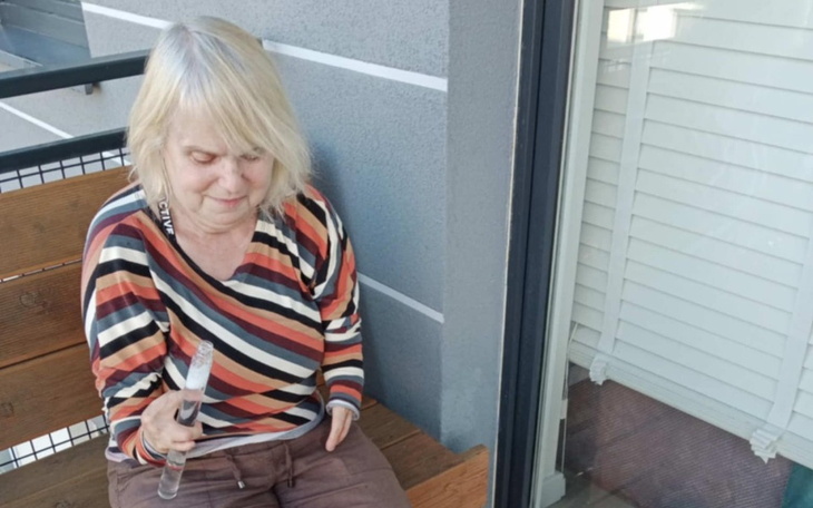 Kobieta w kolorowej bluzce siedząca na balkonie z kijkiem.