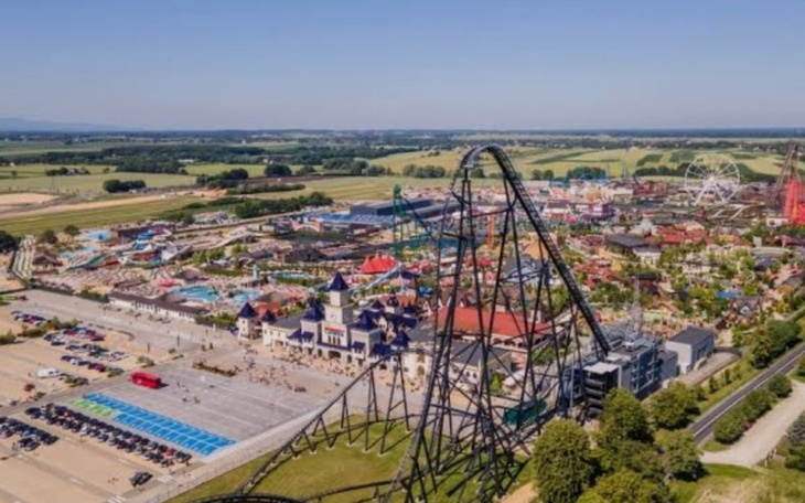 Widok na park rozrywki z rollercoasterem i atrakcjami w tle.