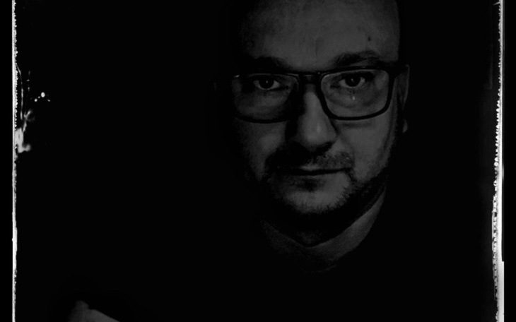 Człowiek w ciemności, z okularami, patrzący w obiektyw.