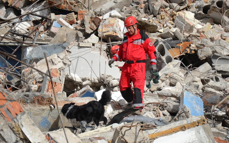 Ratownik w czerwonym stroju z psem wśród gruzów.