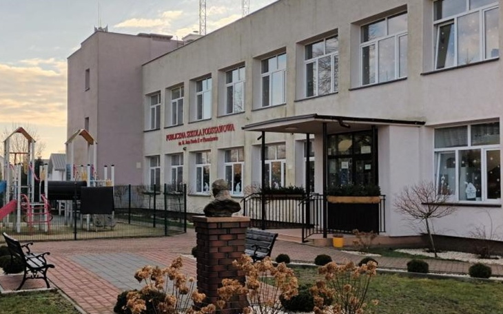 Widok na szkołę podstawową z placem zabaw i ogrodem.