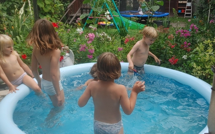 Dzieci bawiące się w basenie w ogrodzie pełnym kwiatów.