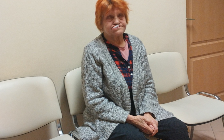 Starsza kobieta siedząca na krześle, z nietypową fryzurą.