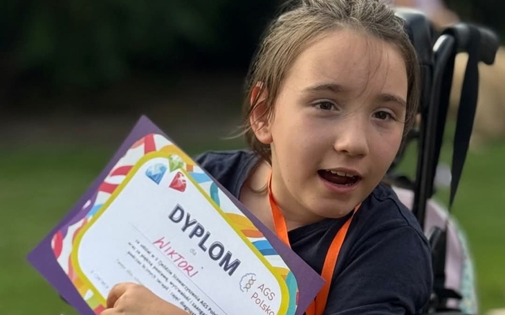 Dziewczynka z dyplomem, uśmiechająca się do kamery.