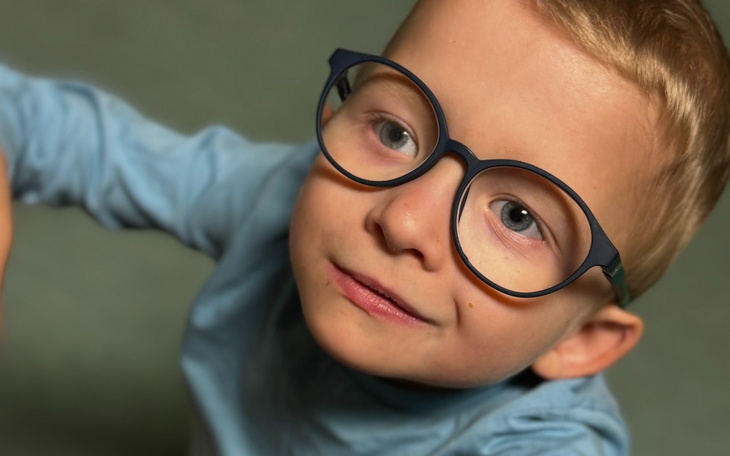 Chłopiec w okularach, patrzący w górę z uśmiechem.