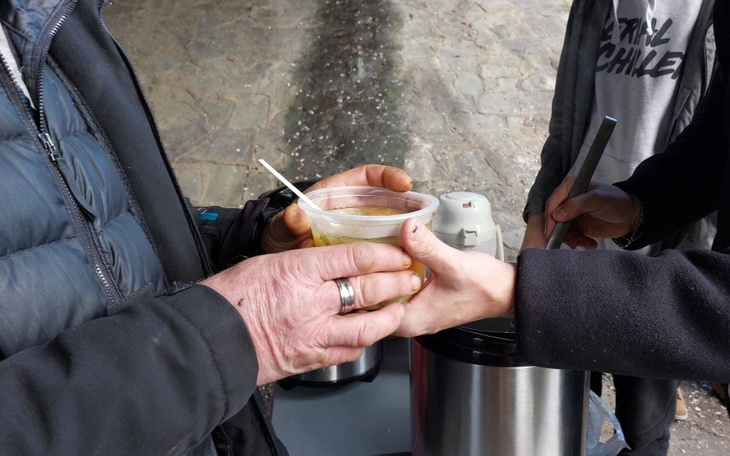 Osoba trzymająca kubek z napojem, pomoc dla potrzebujących.