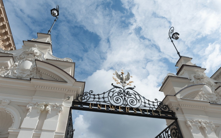 Brama uniwersytetu z piękną architekturą i niebem w tle.