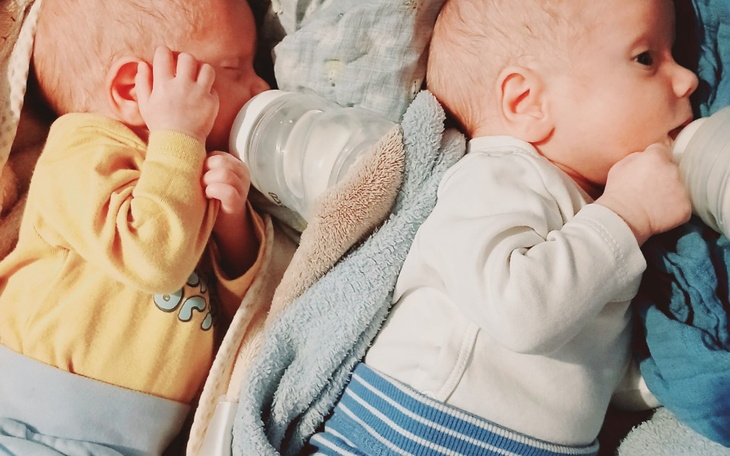 Dwa niemowlęta pijące z butelek, otulone w kocyki.