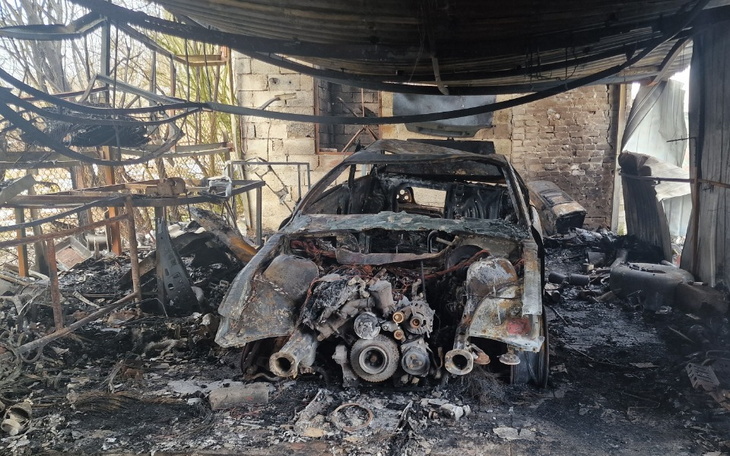 Zniszczony samochód w opuszczonym warsztacie, otoczony popiołem.