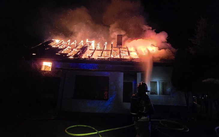 Pożar dachu budynku, strażak walczy z ogniem w nocy.