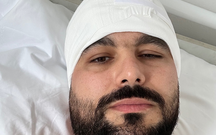 Mężczyzna w łóżku szpitalnym z opatrunkiem na głowie.