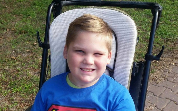 Chłopiec w niebieskiej koszulce, uśmiechający się na wózku.