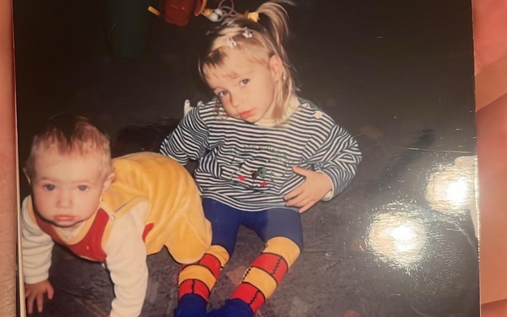 Dzieci bawiące się na podłodze, jedno w żółtej spódnicy, drugie w pasiaku.