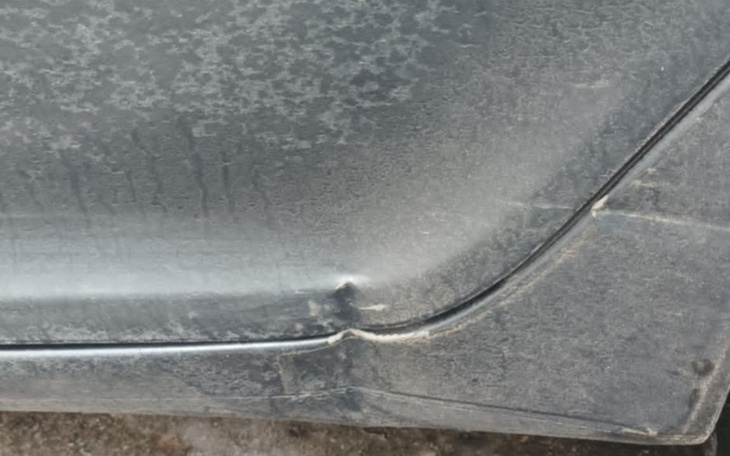 Zbliżenie na zarysowany bok samochodu, pokryty kurzem.