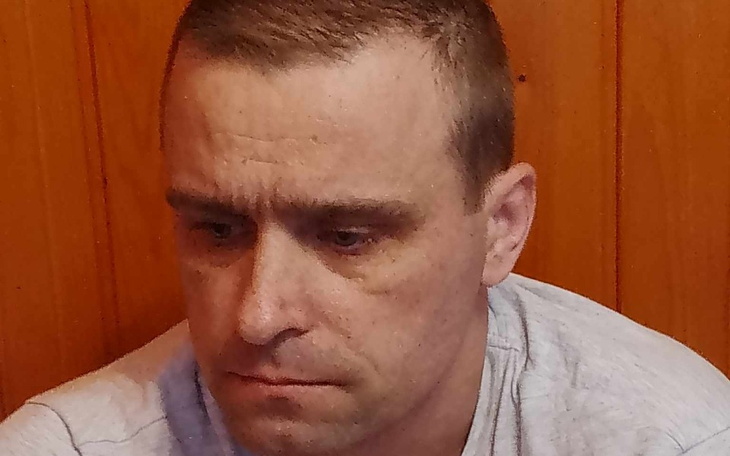 Mężczyzna z zamyśloną miną, siedzi w drewnianym pomieszczeniu.