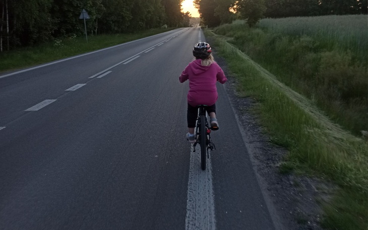Dziecko na rowerze, jedzie wzdłuż drogi w czasie zachodu słońca.