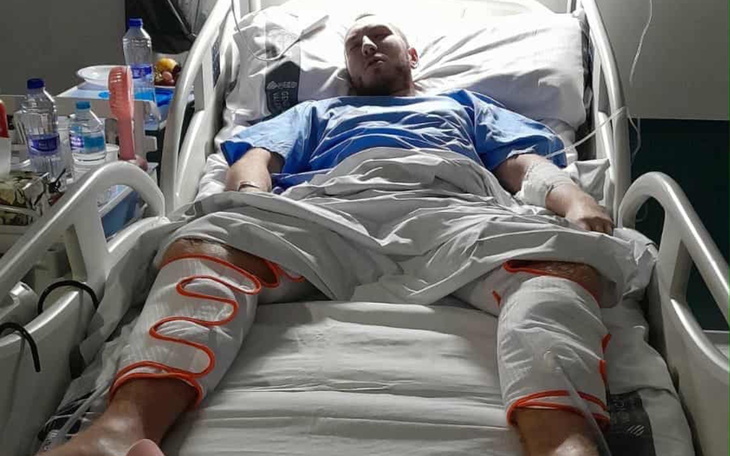 Mężczyzna leżący w szpitalnym łóżku, z opatrunkami na nogach.