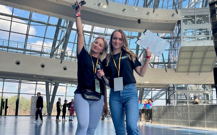 Dwie dziewczyny w trakcie wydarzenia, uśmiechnięte i trzymające mikrofony.