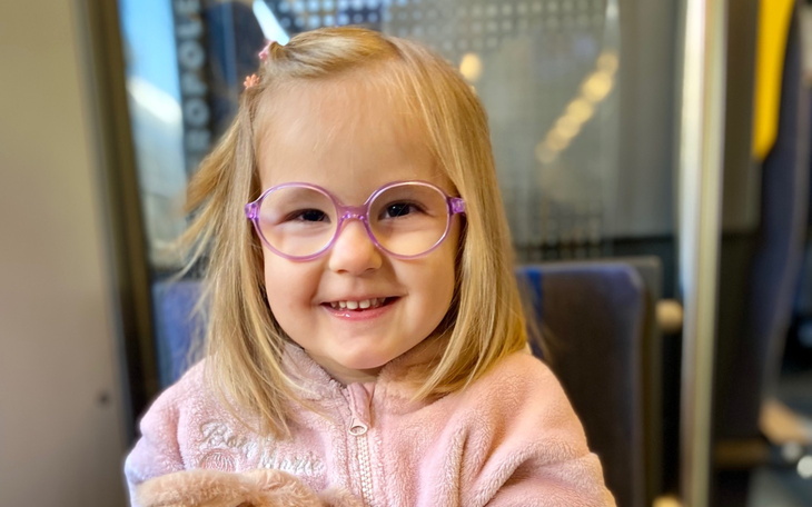 Uśmiechnięta dziewczynka w okularach, siedząca w pociągu.