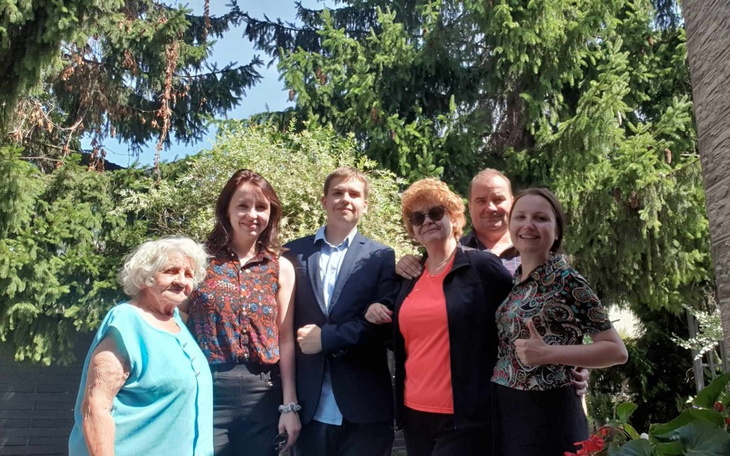 Grupa ludzi pozująca do zdjęcia w ogrodzie, w słoneczny dzień.