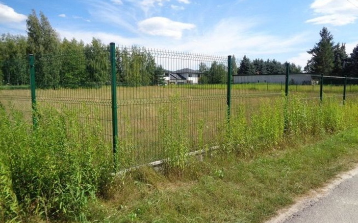 Pusty teren ogrodzony siatką, z domem w tle.