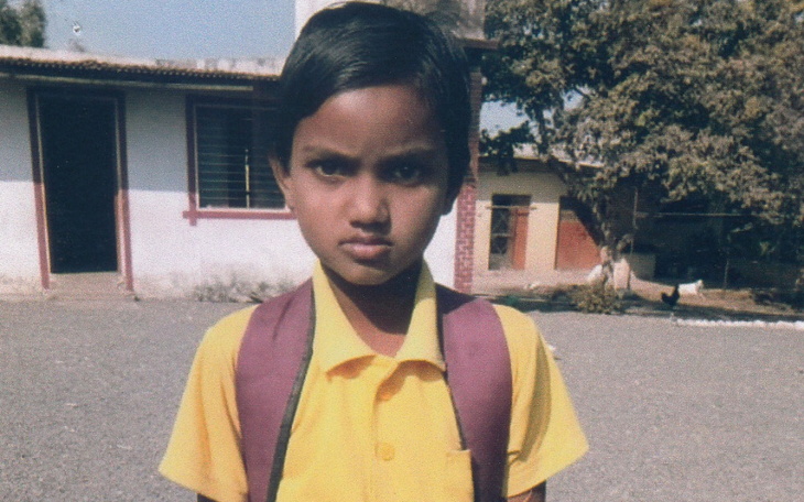 Chłopiec w żółtej koszulce z plecakiem, patrzy w obiektyw.