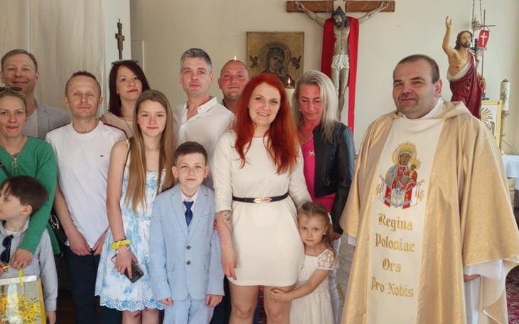 Rodzina pozująca z księdzem w kościele.