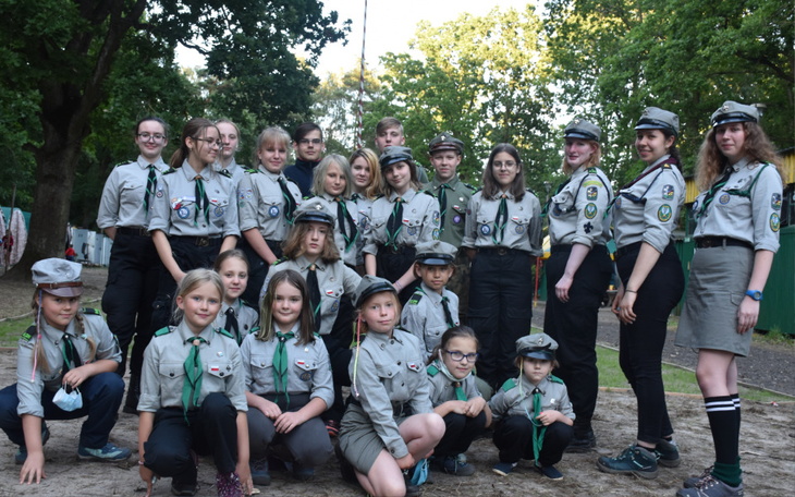 Grupa harcerzy w mundurach, pozująca na tle drzew.
